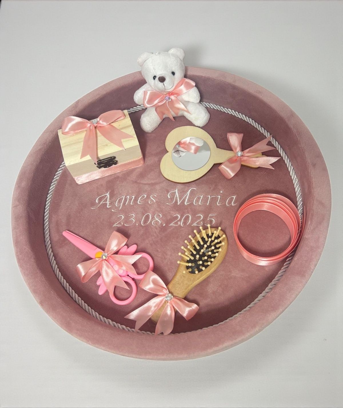 Tavă din catifea roz cu un ursuleț de pluș, o cutie mică, o oglindă, o perie de păr și o foarfecă.