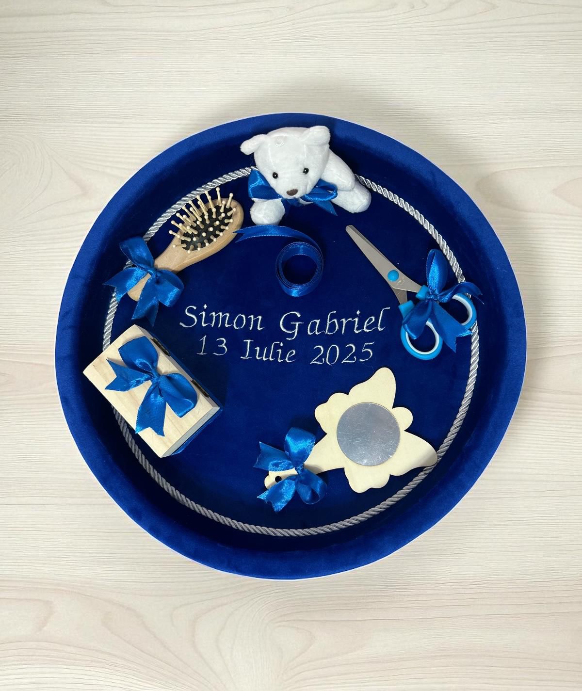Tavă din catifea albastră cu numele Simon Gabriel și data 13 Iulie 2025, decorată cu diverse obiecte.